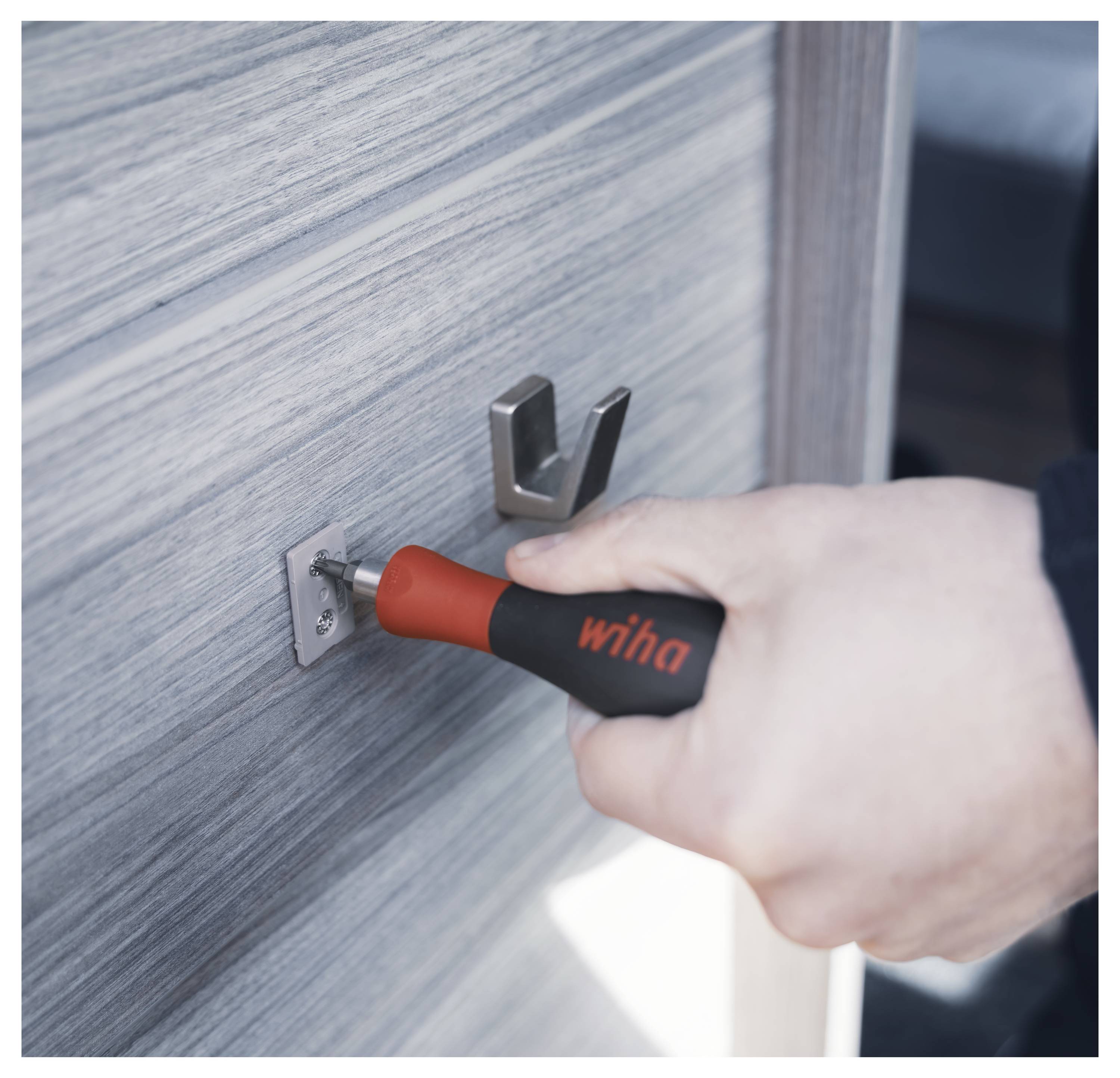 Eine Hand verwendet einen Wiha-Schraubendreher, um eine Schraube an einer Metallhalterung zu festigen, die auf einer Holzoberfläche befestigt ist.