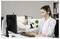 Eine Frau, die ein Headset trägt, arbeitet an einem Computer in einem Büro. Sie ist konzentriert, umgeben von Papieren, einer Pflanze und Büromaterialien.
