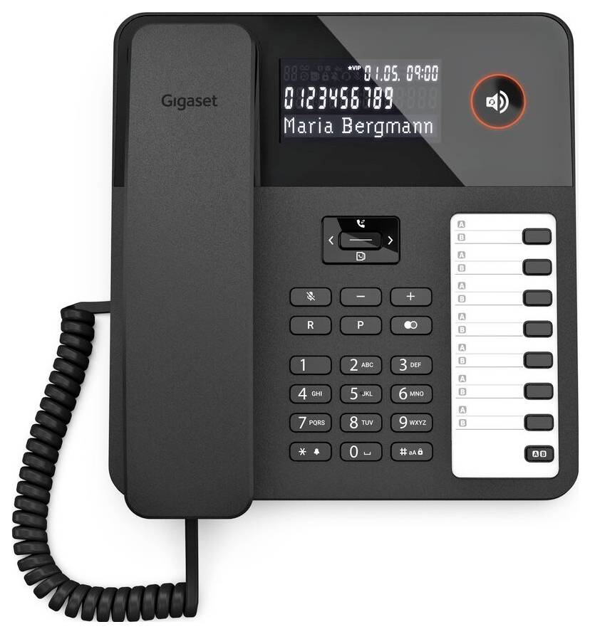 Ein schwarzes Büro-Festnetztelefon mit digitalem Display, das die Uhrzeit '09:00' und den Namen 'Maria Bergmann' anzeigt. Numerische Tastatur und Schnellwahlschaltflächen sind sichtbar.