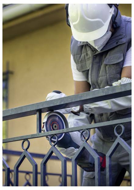 Ein Bauarbeiter in Schutzausrüstung benutzt einen Winkelschleifer, um durch ein Metallgeländer zu schneiden, was die Sicherheit bei der Bauarbeit unterstreicht.