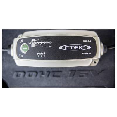 Ein Autobatterie-Ladegerät mit der Bezeichnung "CTEK MXS 3.8" mit Modustaste und Indikatoren für Ladestufen steht auf einer strukturierten Oberfläche.