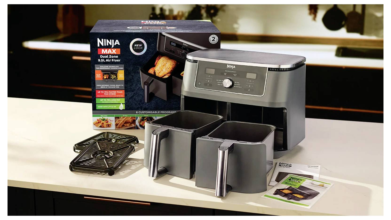 „Ninja Max Dual Zone 8-Qt. Heißluftfriteuse" mit Verpackung, die zwei Kochschalen und ein Rezeptbuch auf einer Küchentheke zeigt.
