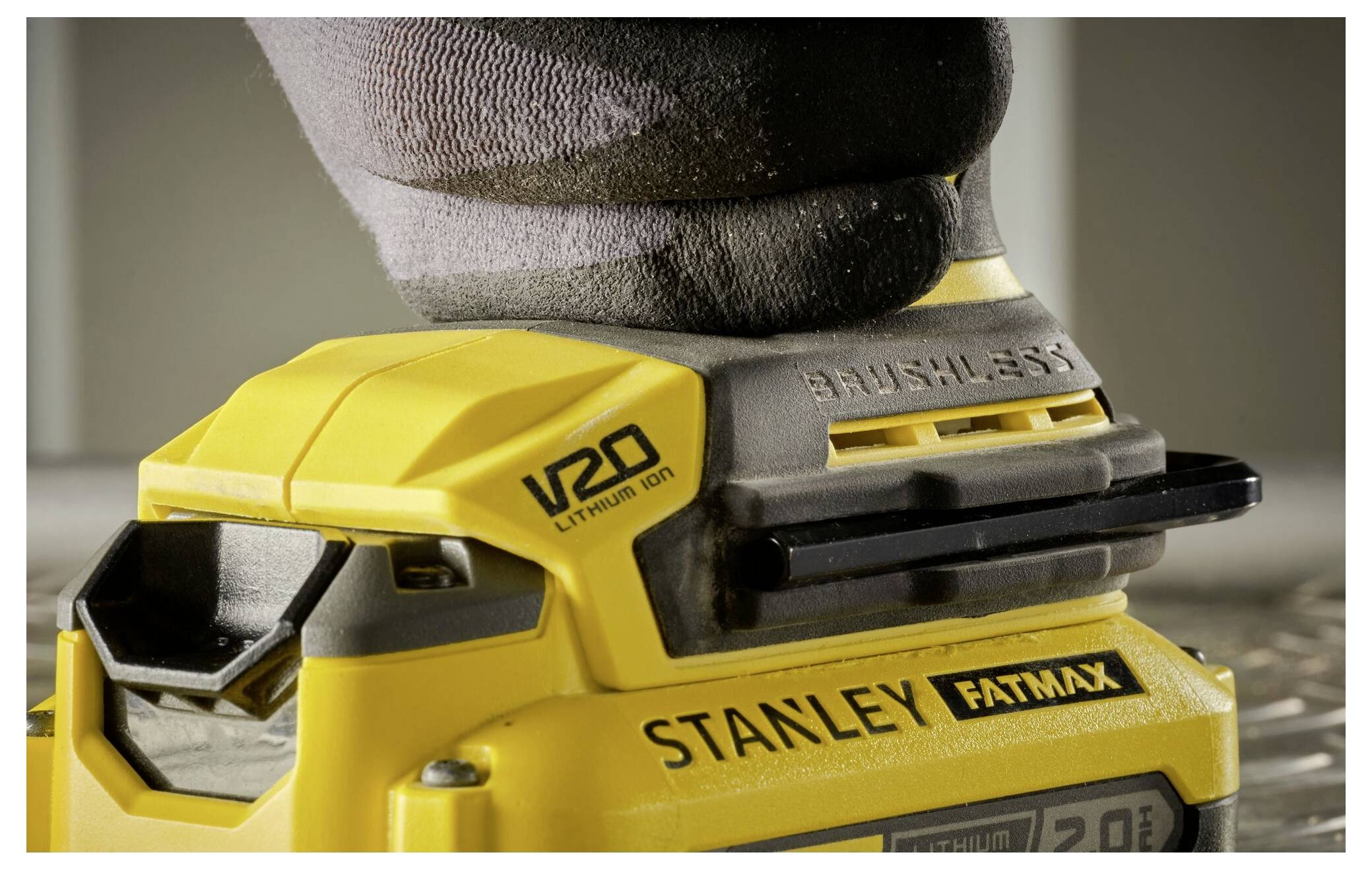 Eine behandschuhte Hand bedient ein gelbes kabelloses Stanley-Werkzeug mit bürstenlosen Motoren auf einer Oberfläche. Das Werkzeug trägt die Kennzeichnung „V20 Lithium Ion".
