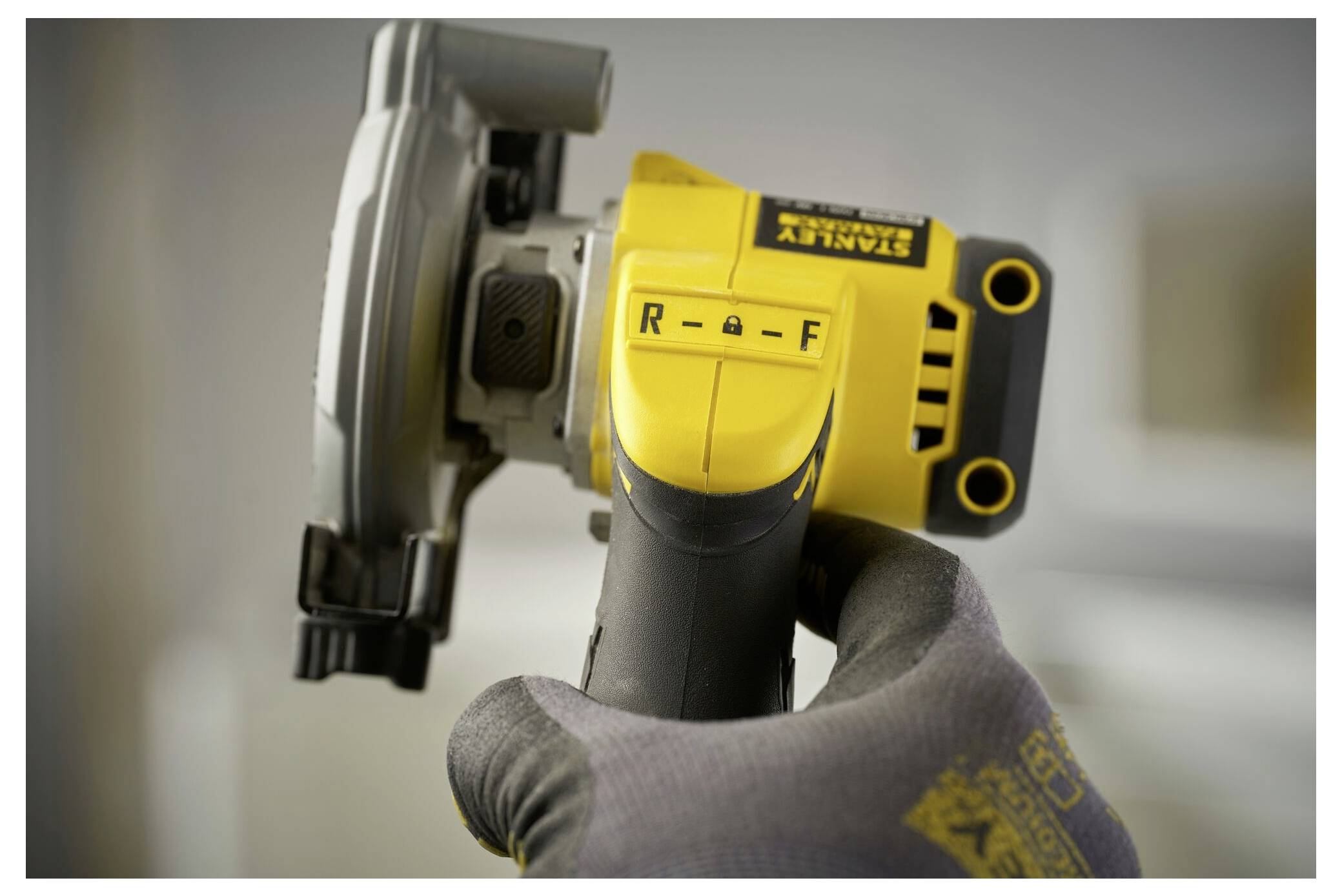 Eine behandschuhte Hand hält ein Stanley-Elektrowerkzeug mit gelbem und grauem Gehäuse und konzentriert sich auf einen Schalter mit den Beschriftungen „R" und „F" für Rückwärts und Vorwärts.