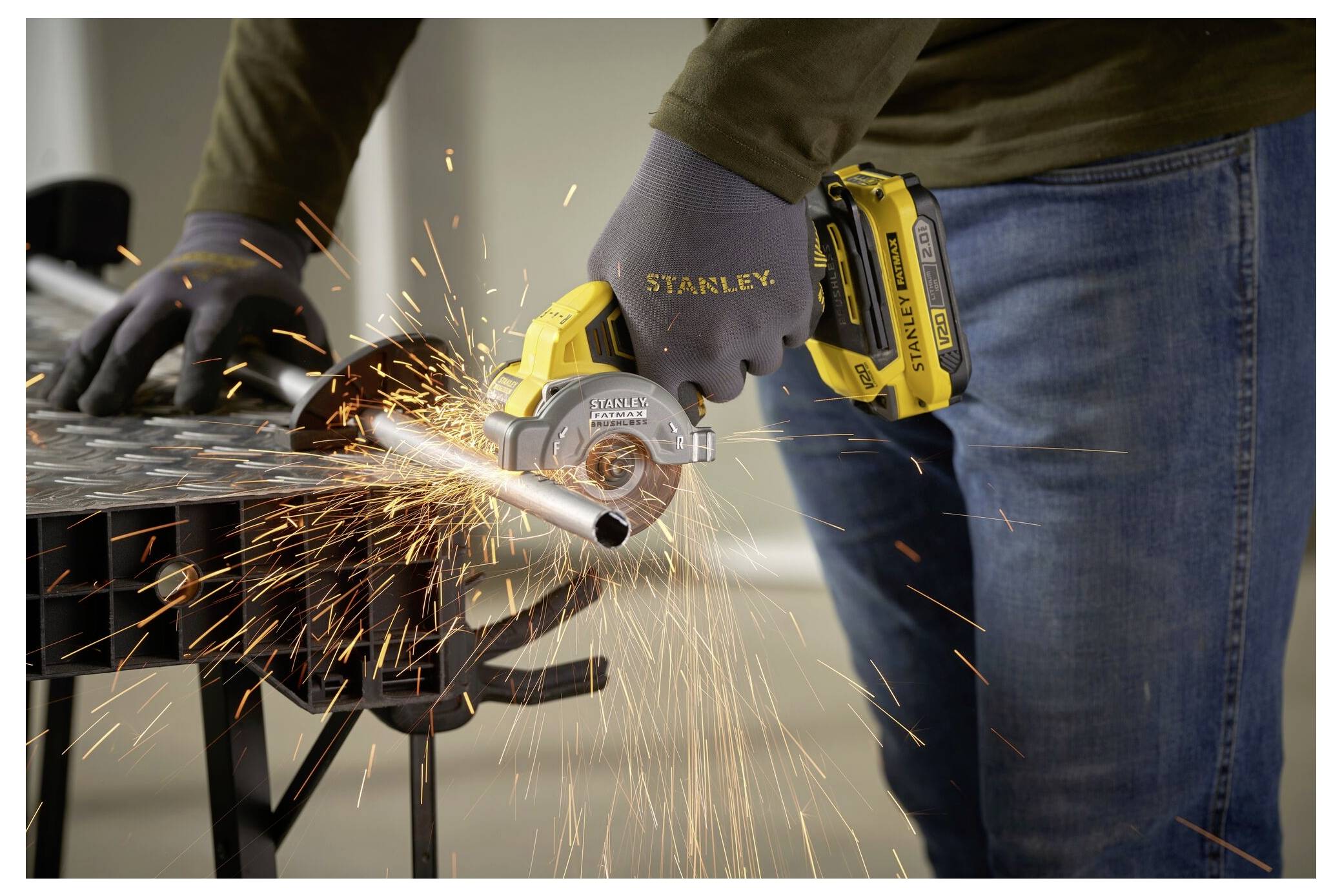 Eine Person in Handschuhen benutzt ein Elektrowerkzeug, um ein Metallrohr zu schneiden, wobei Funken fliegen. Das Werkzeug ist batteriebetrieben und trägt die Marke „Stanley".