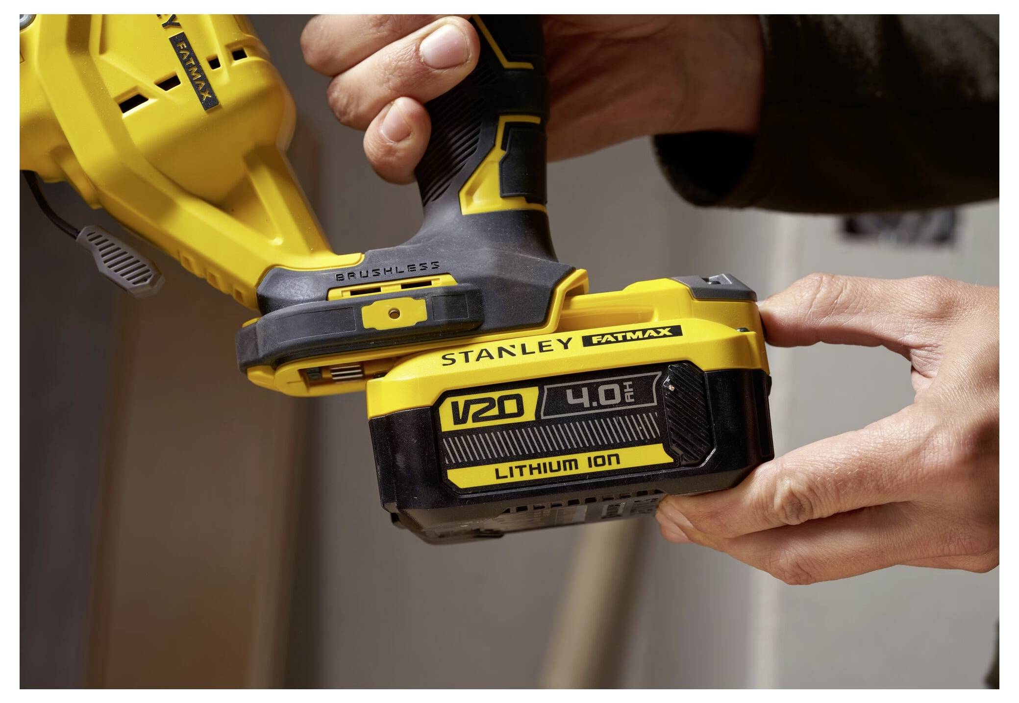 Eine Person hält ein gelbes kabelloses Werkzeug der Marke "Stanley Fatmax" mit sichtbarem "V20 4.0Ah Lithium Ion" Akku.