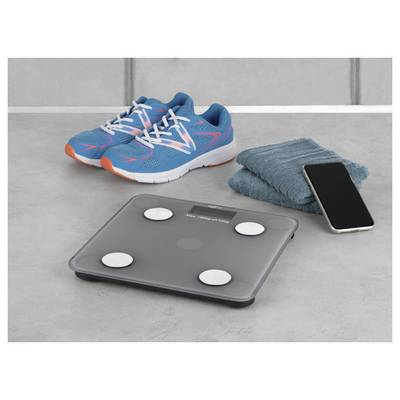 Eine digitale Badezimmerwaage neben einem Smartphone, blaue Sportschuhe und ein gefaltetes Handtuch auf einer grauen Oberfläche.