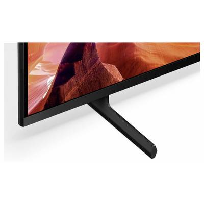 Nahaufnahme der unteren Ecke eines Flachbildfernsehers und des V-förmigen Ständers auf weißem Hintergrund, die die dünne Blende des Displays und die Stützbasis zeigen.