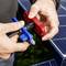 Hände verbinden rote und blaue MC4-Solarpanel-Kabelstecker neben einem Photovoltaik-Panel.
