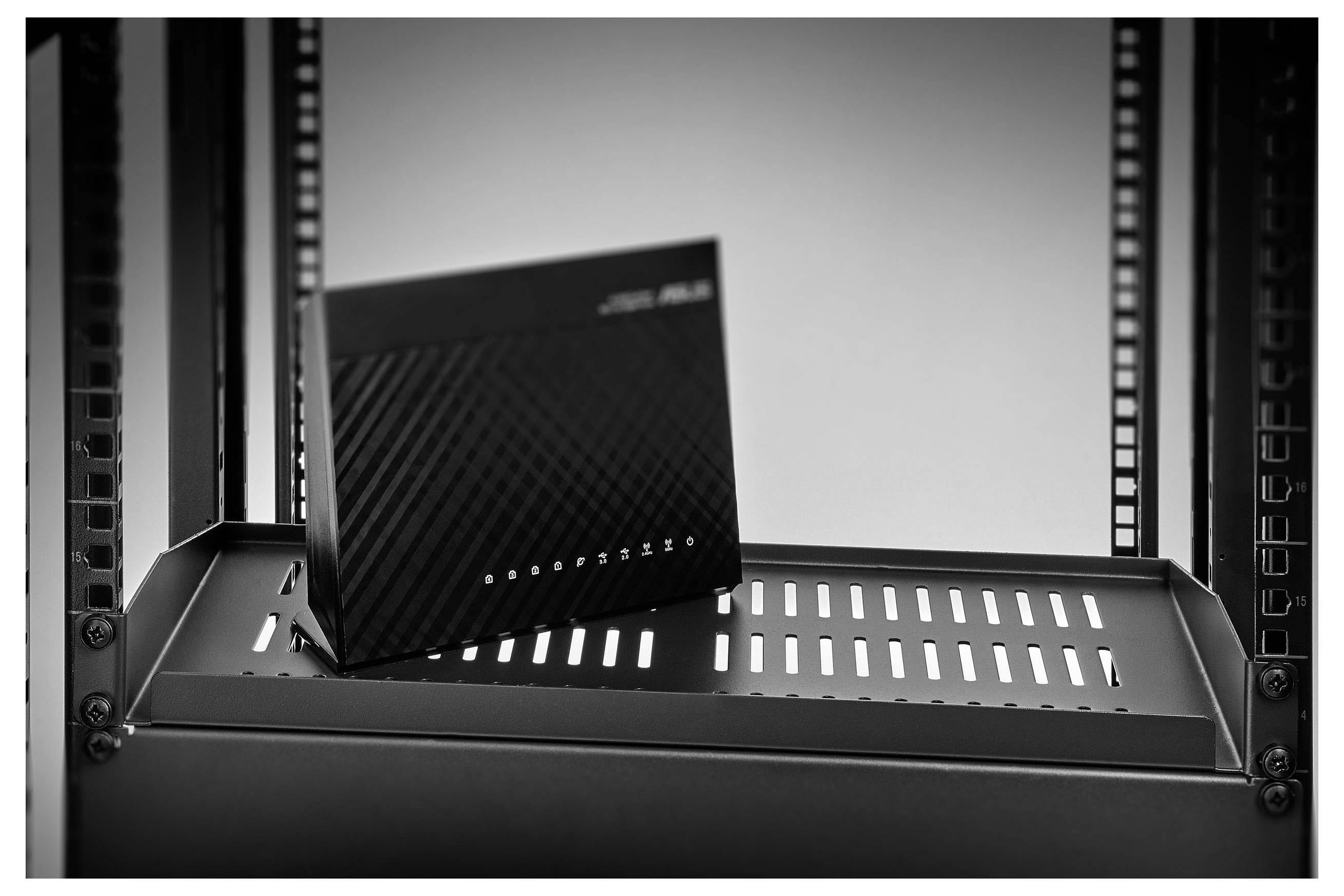Kleines schwarzes ASUS-Netzwerkgerät, das auf einem Metallserverregal-Regalbrett zwischen Schrankschienen steht.