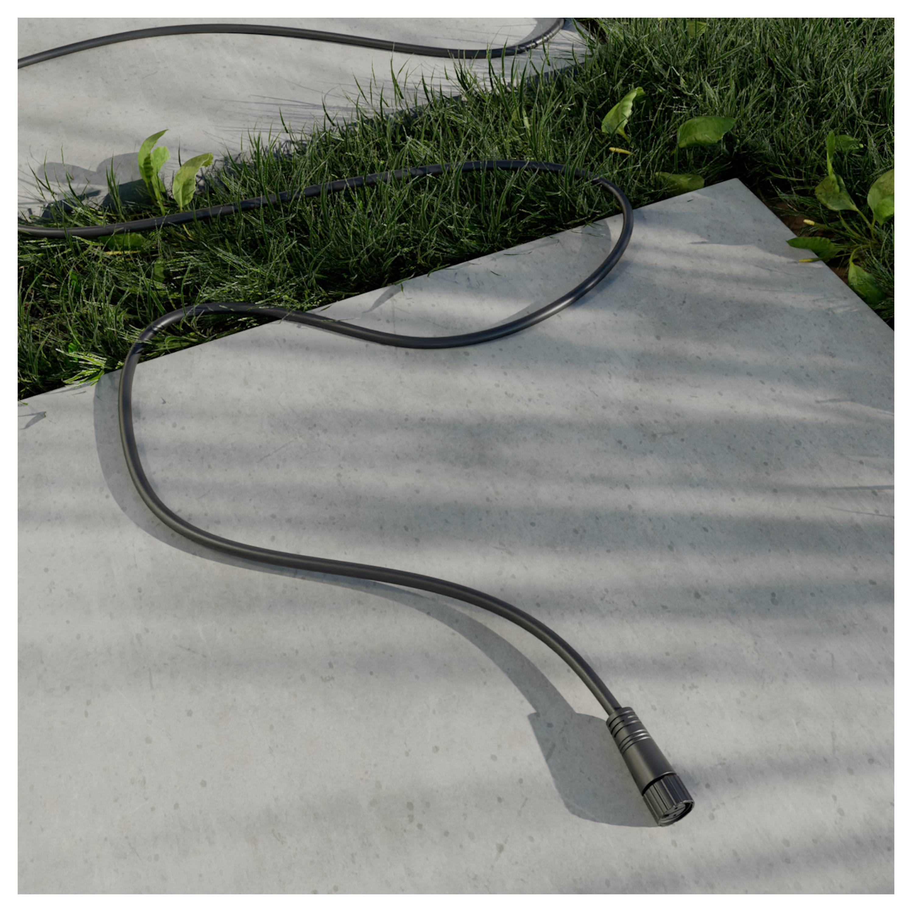 Schwarzes Kabel auf einem Betonweg neben Gras liegend, mit einem Steckerende im Vordergrund.