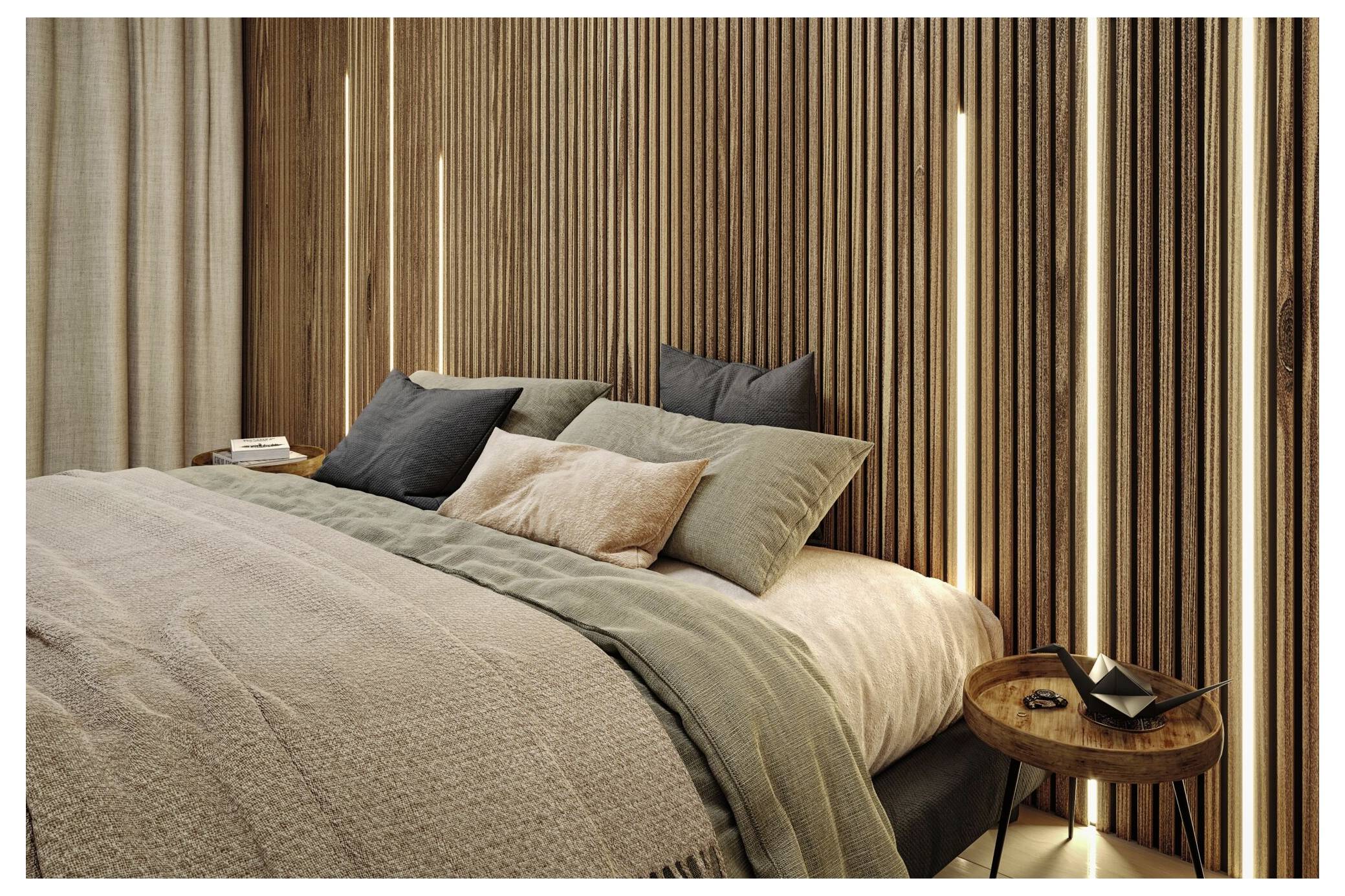 Ein ordentlich gemachtes Bett mit geschichteter neutraler Bettwäsche und Kissen neben einem kleinen runden Holznachttisch in einem warmen, modernen Schlafzimmer.