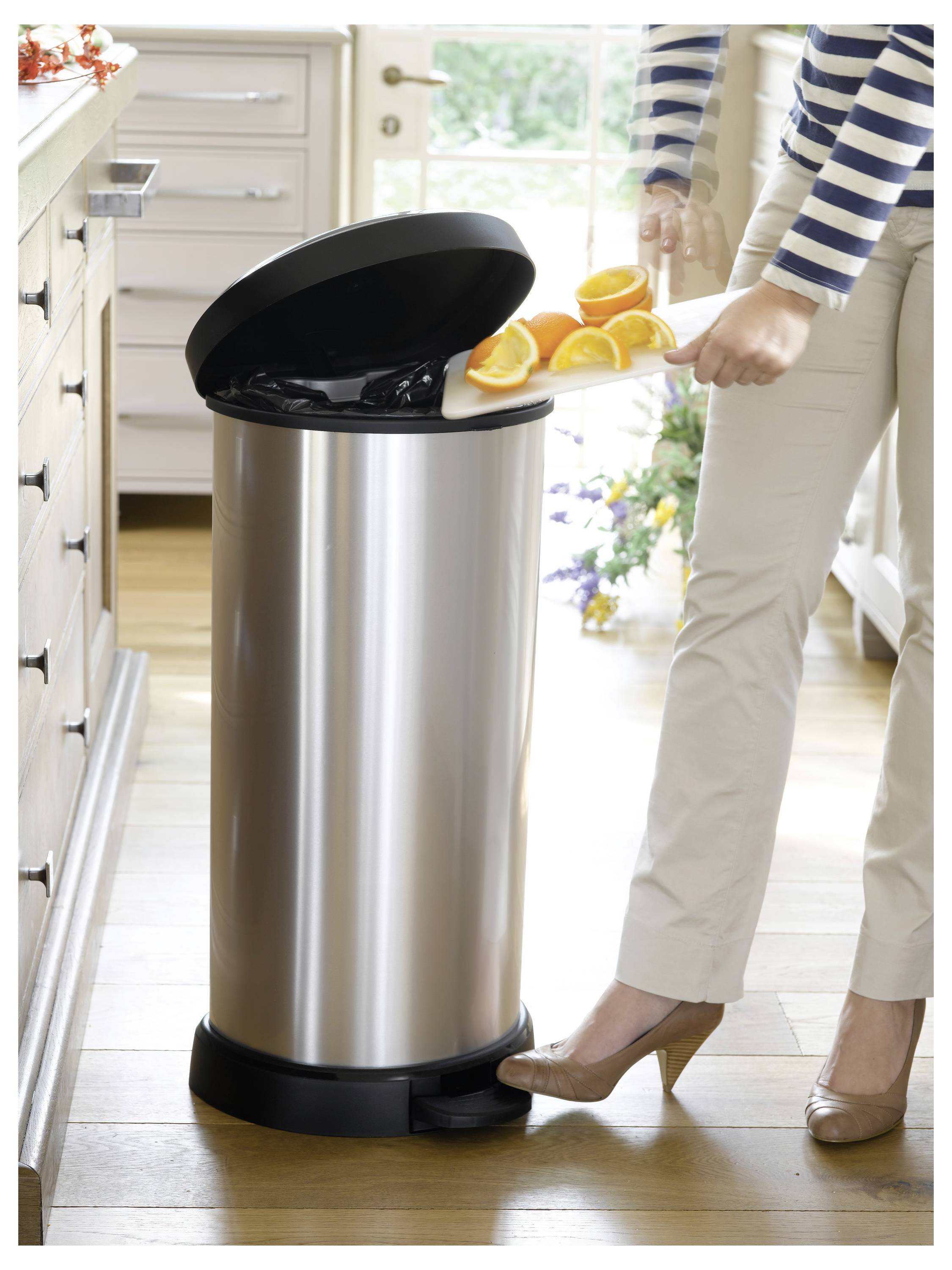 Person benutzt einen Edelstahl-Tretmülleimer, um Orangenschalen in einer hellen Küche zu entsorgen.