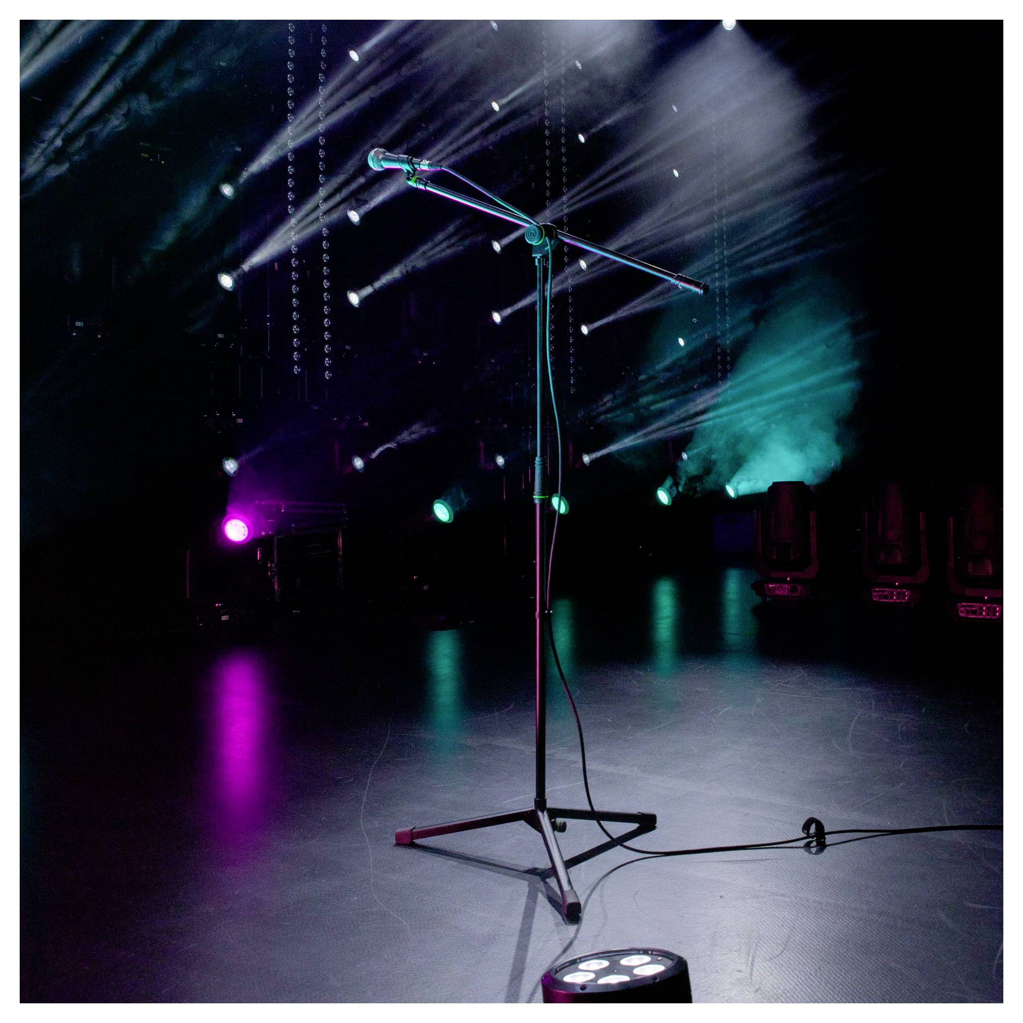 Leeres Mikrophonständer auf einer dunklen Konzertbühne mit farbigen Scheinwerfern und Nebel, was ein Live-Performance-Setup andeutet.