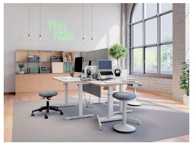 Modernes offenes Büro mit Schreibtischen, Computern, Hockern und Regalen unter einem Neon-Schild „FEEL GOOD" neben großen Fenstern.