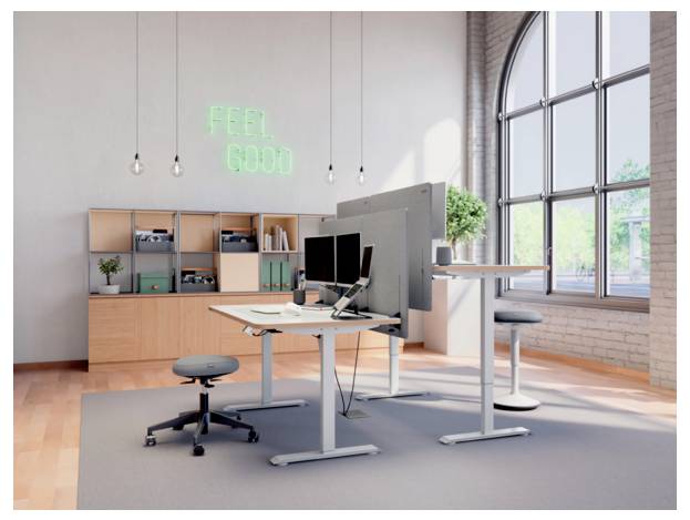 Modernes Open Office mit Sitz-Steh-Schreibtischen, Monitoren, Regalen und einem Neon-Schild mit der Aufschrift „FEEL GOOD" neben großen Bogenfenstern.
