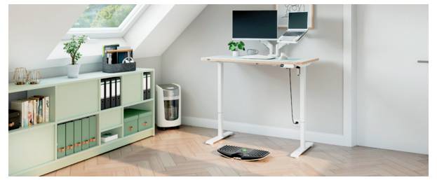 Minimales Homeoffice in einem Dachzimmer, mit einem Stehschreibtisch, Monitor und Laptop, Aufbewahrungsschrank, Pflanzen und einer Tastatur auf dem Boden.