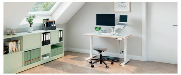 Minimales Homeoffice mit weißem Schreibtisch, Computermonitor, Laptop, Hocker und mintfarbener Aufbewahrungsschrank unter einem Oberlicht in einem Raum mit Schrägdach.