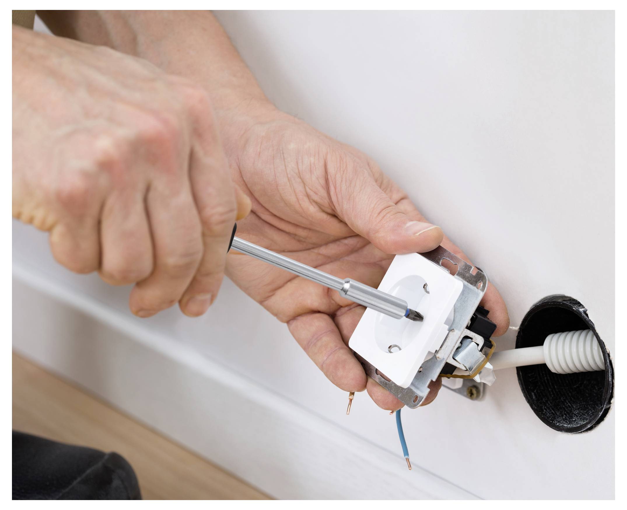 Hände installieren eine elektrische Wandsteckdose mit einem Schraubendreher, freiliegende Drähte sind in der Nähe einer Wandöffnung sichtbar.
