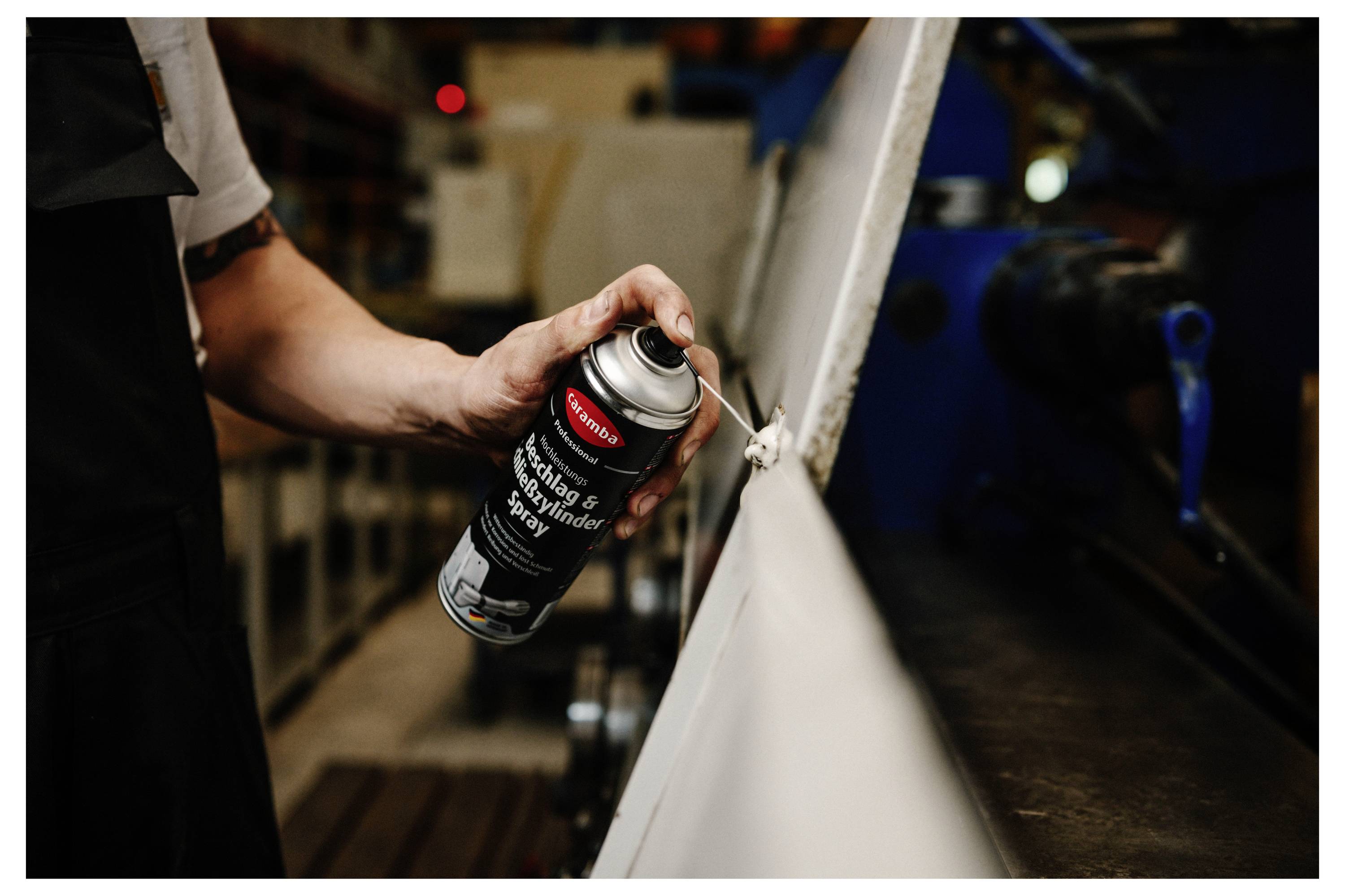 Dose mit „Caramba Professional" Edelstahl-Schlosszylinder-Spray auf einem Werkstatttisch, umgeben von Metallteilen und Werkzeugen.