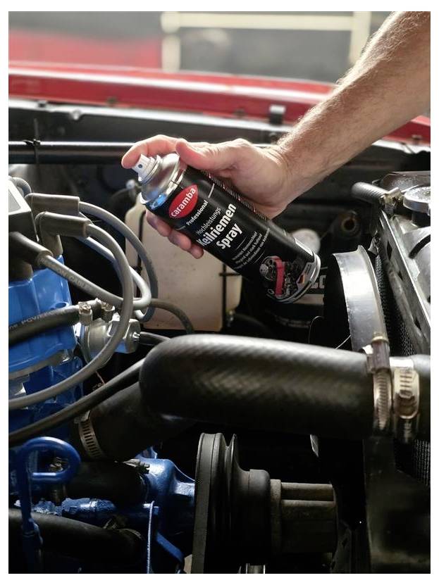Mit einer Dose „Silikonspray" wird Schmiermittel mit der Hand in einen Motorraum eines Autos gesprüht.