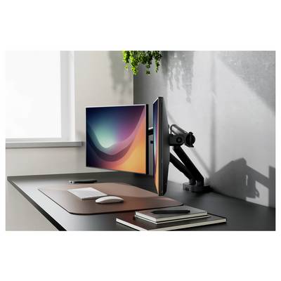 Modernes Schreibtischset-up mit zwei Monitoren auf einem verstellbaren Arm, Tastatur und Maus auf einer Matte, sowie Notizbüchern und einem Telefon neben einem Fenster.