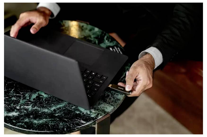 Geschäftsmann, der an einem Tisch einen Laptop nutzt und eine Kreditkarte durchzieht, was auf eine Online-Zahlung oder einen Online-Kauf hindeutet.