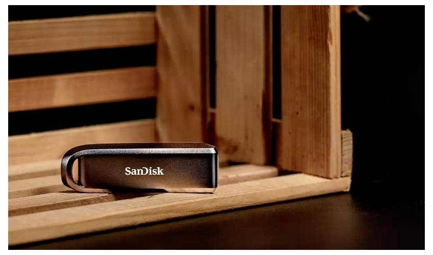 SanDisk USB-Speicherstick auf einer Holzoberfläche neben einer kistenartigen Holzkonstruktion