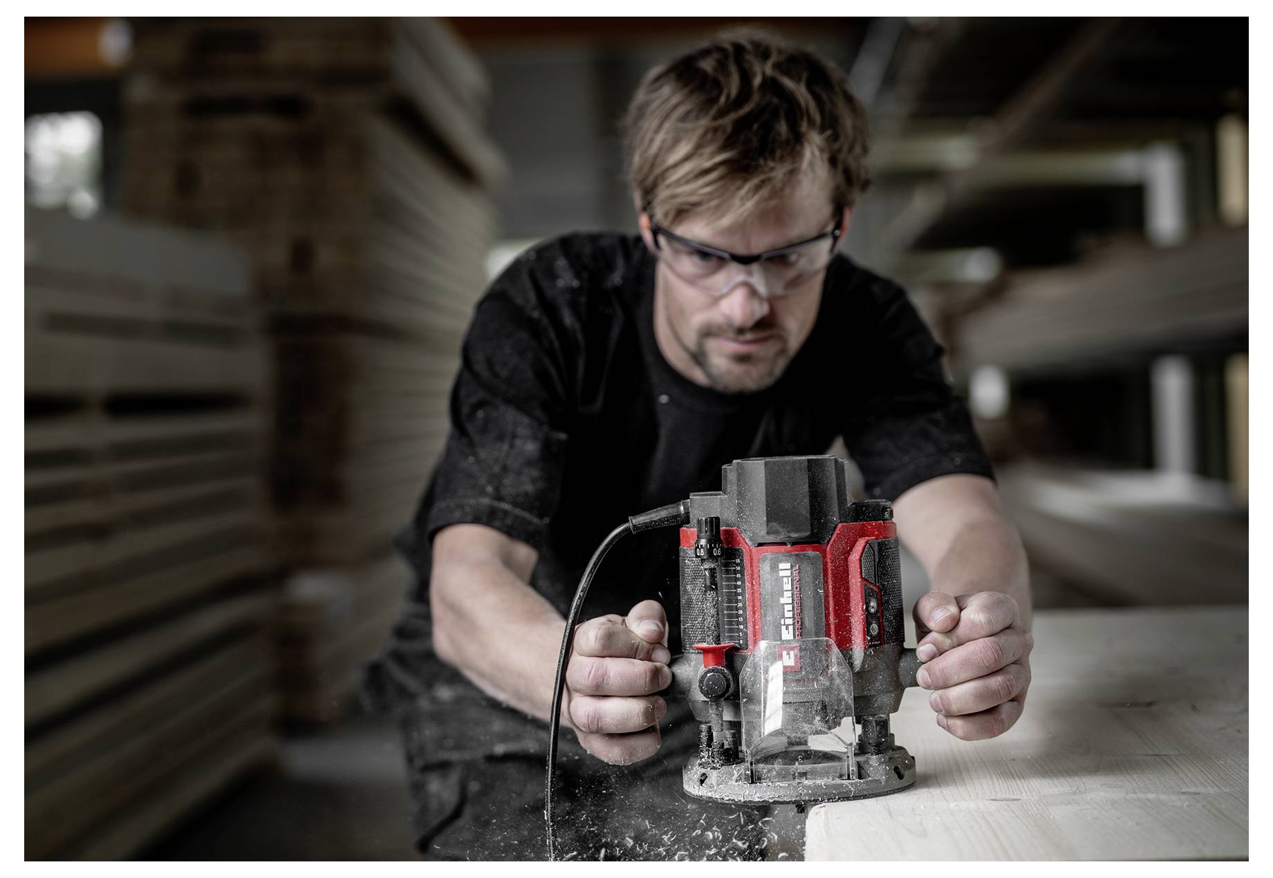 Ein Mann mit einer Schutzbrille verwendet einen rot-schwarzen Elektroschlei­fer, um Holz in einer Werkstatt zu schneiden.