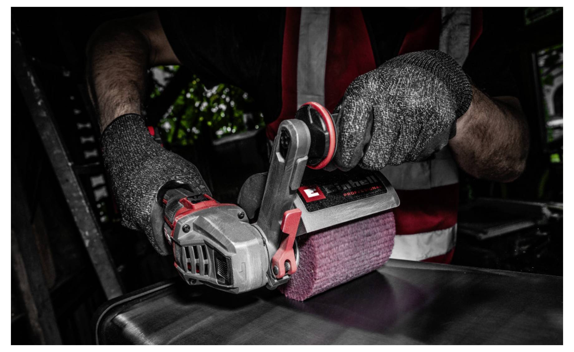 Handschuhgetragener Arbeiter, der einen tragbaren elektromechanischen Schleiffer verwendet, um eine dunkle Metalloberfläche in einer Werkstatt zu glätten.