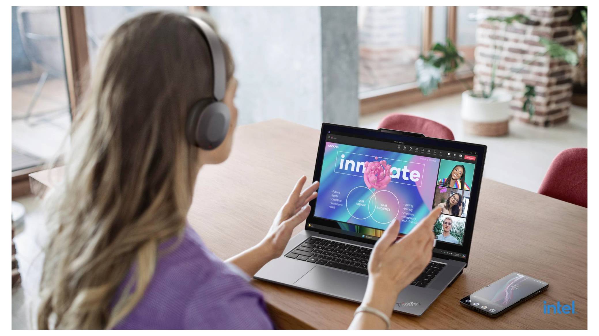 Frau mit Kopfhörern nimmt an einer Videokonferenz auf einem Laptop teil, auf dem „innovate" und mehrere Teilnehmer-Miniaturansichten angezeigt werden, während sie an einem Tisch sitzt.