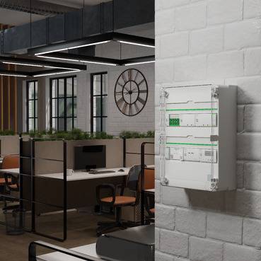Wandmontierte elektrische Schalttafel in einem modernen Büroraum mit Arbeitsplätzen und einer Wanduhr im Hintergrund.