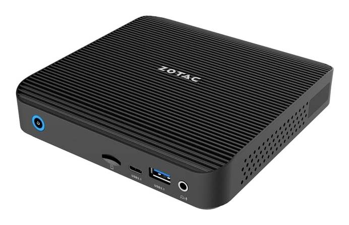Kompakter Zotac Mini-PC mit geripptem schwarzem Gehäuse, vorderer Einschalttaste, USB-Anschlüssen und Audio-Buchse auf weißem Hintergrund.