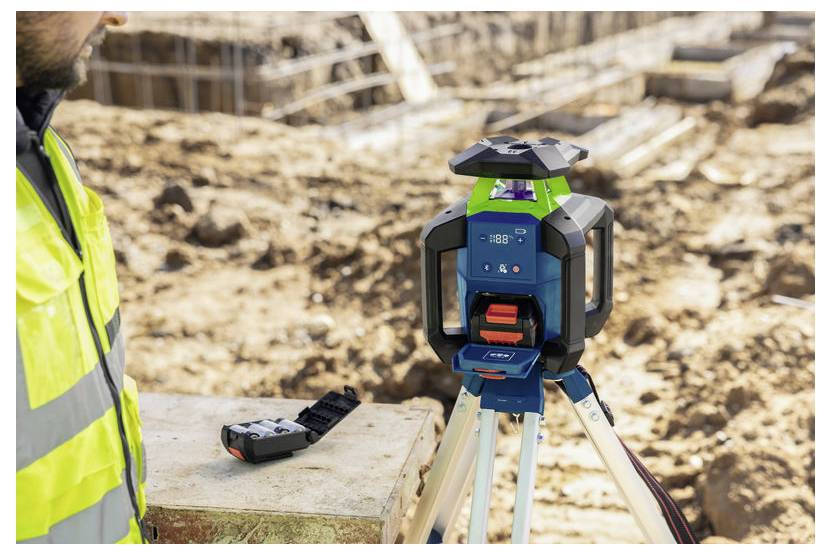 Bauarbeiter neben einem dreibeinigen Laser-Nivelliergerät auf einer Baustelle, was auf Vermessung oder Nivellierung während einer Ausschachtung hinweist.