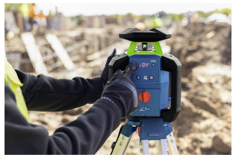 Ein Arbeiter stellt ein blaues Konstruktions-Laserniveau auf einem Stativ auf einer Baustelle ein.