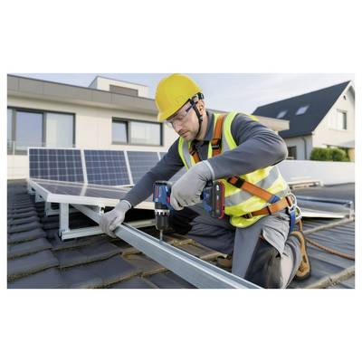 Arbeiter in Schutzausrüstung installiert Solarpaneele auf einem Dach mit einer Elektrobohrmaschine, während Wohngebäude im Hintergrund zu sehen sind.