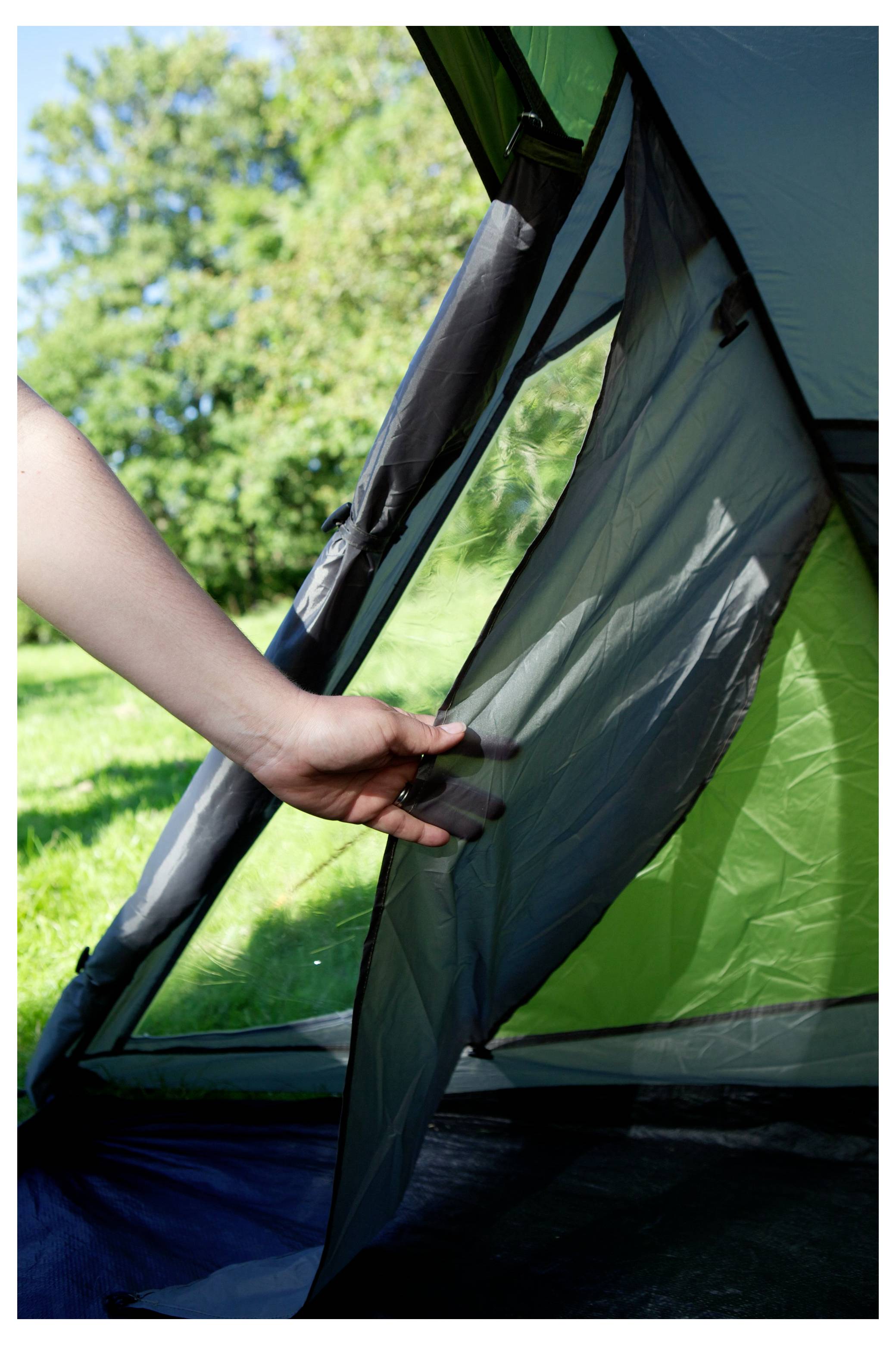 Hand, die die Netztür eines grünen Campingzelts im Freien in einem grasbewachsenen Bereich mit Bäumen im Hintergrund öffnet.