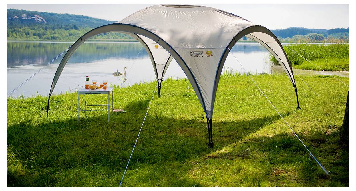 Pavillon-Zelt auf einem grasbewachsenen Seeufer aufgebaut, mit einem kleinen Tisch und Getränken daneben.