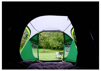 Aussicht von innen aus einem Zelt durch den offenen Eingang auf einen grünen Campingplatz mit Bäumen und einem kleinen Tisch oder Stuhl außerhalb.