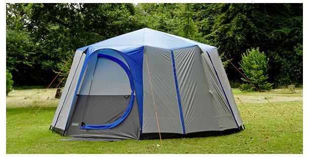 Inneres eines blauen Campingzeltes mit offener Tür, die Gras und eine Steinmauer draußen zeigt.
