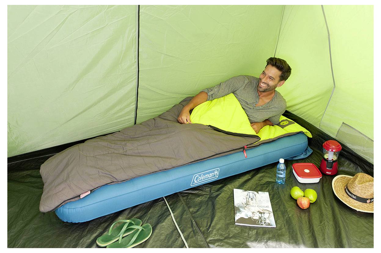 Ein Mann entspannt sich auf einer Schlafmatte in einem grünen Zelt, mit Campingausrüstung und Lebensmitteln in der Nähe.