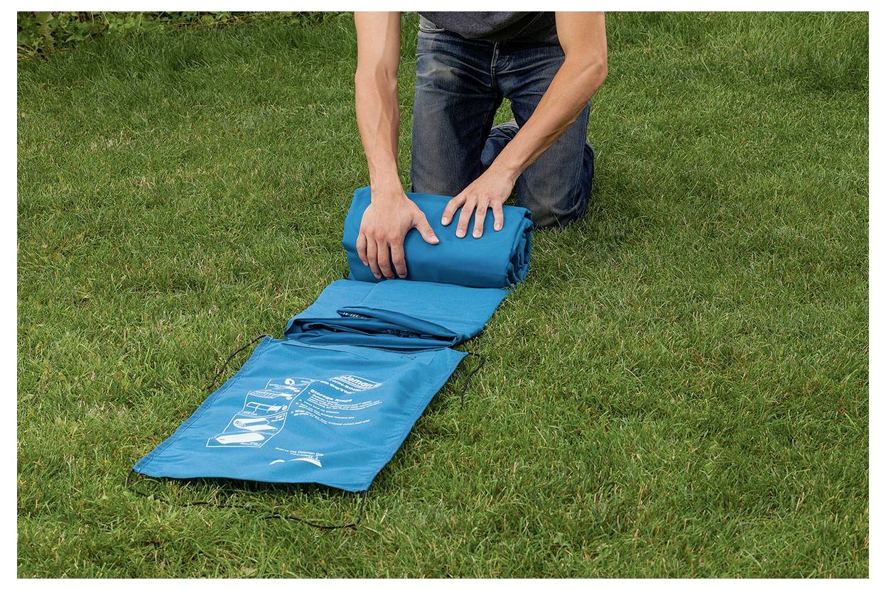 Person rollt eine blaue Schlafmatte oder ein Campingpad auf Gras im Freien auf.