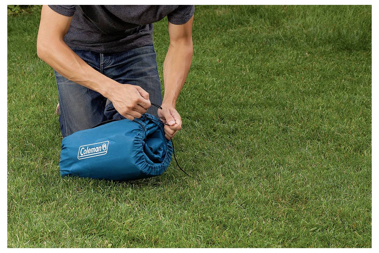 Person zieht an einer Zugschnur, um einen blauen Coleman-Beutel auf Gras im Freien zu packen.