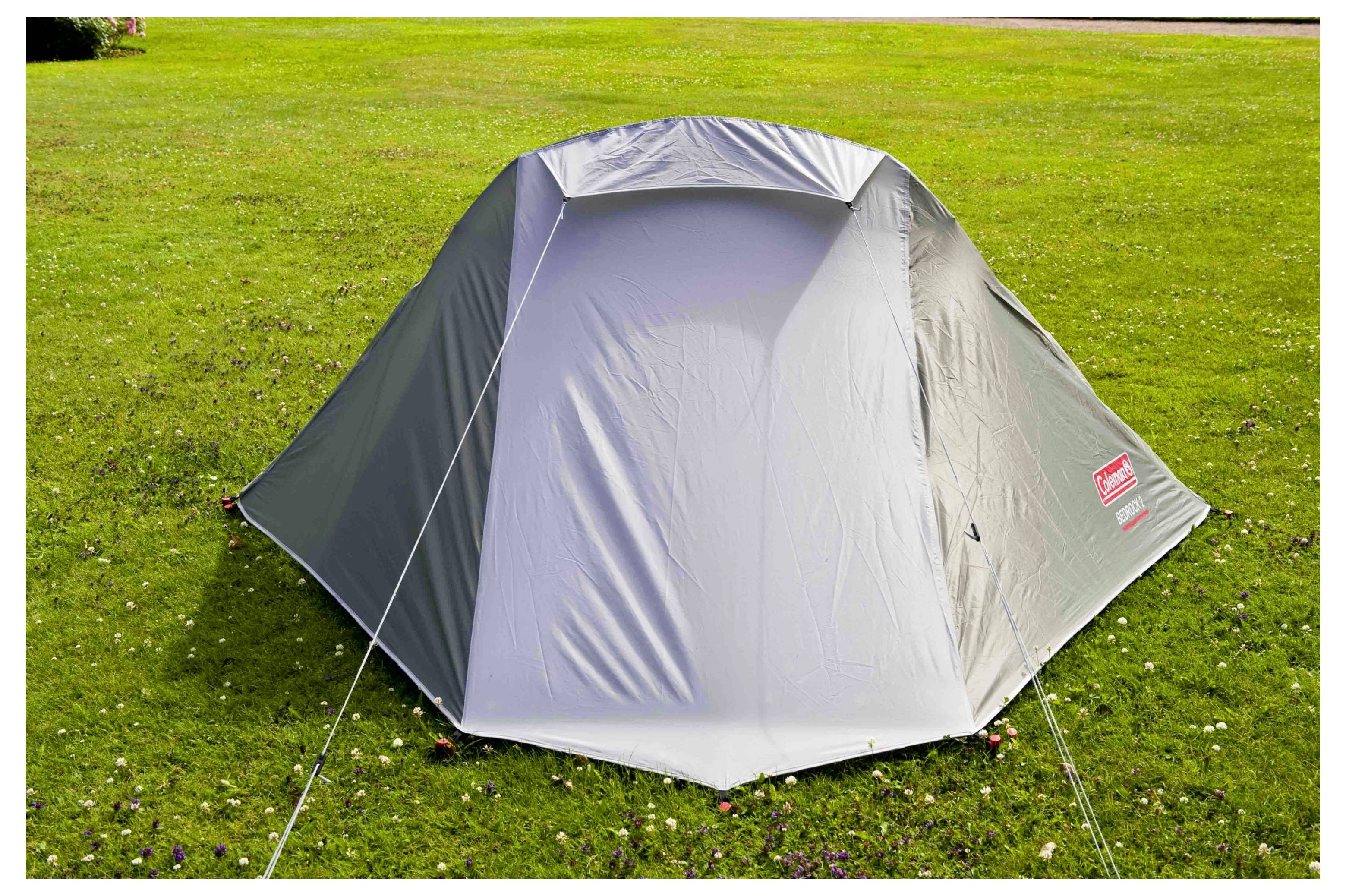 Graues Campingzelt auf einem Grasfeld aufgebaut, von vorne gezeigt mit sichtbaren Spannseilen.