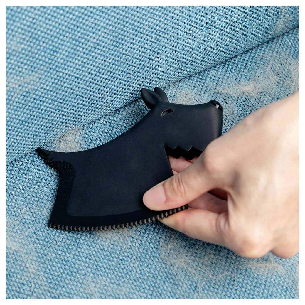 Hand, die einen schwarzen hundeförmigen Fusselentferner benutzt, um Fusseln von einer blauen Stoffoberfläche zu entfernen.