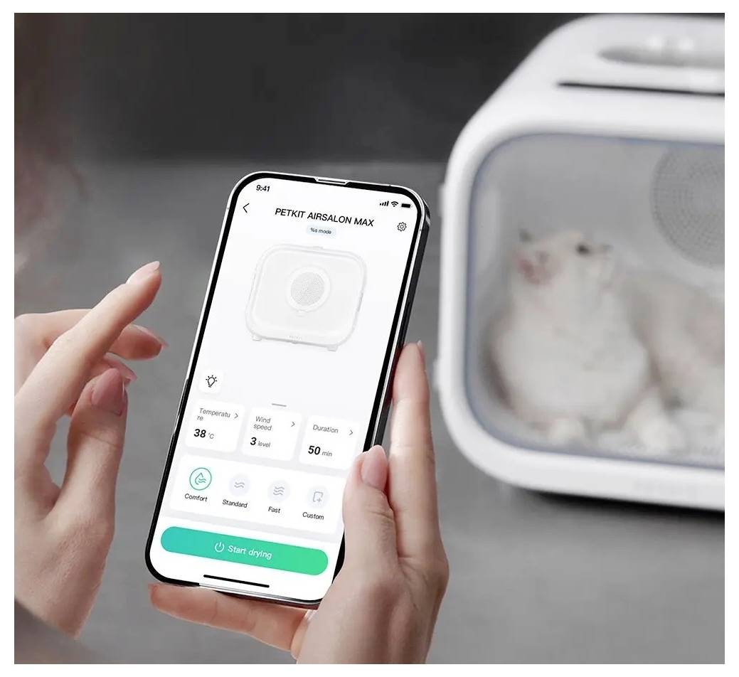 Person nutzt eine Smartphone-App, um einen PETKIT AIRSALON MAX Haartrockner für Haustiere zu steuern, mit einer Katze, die im Trockner sichtbar ist.