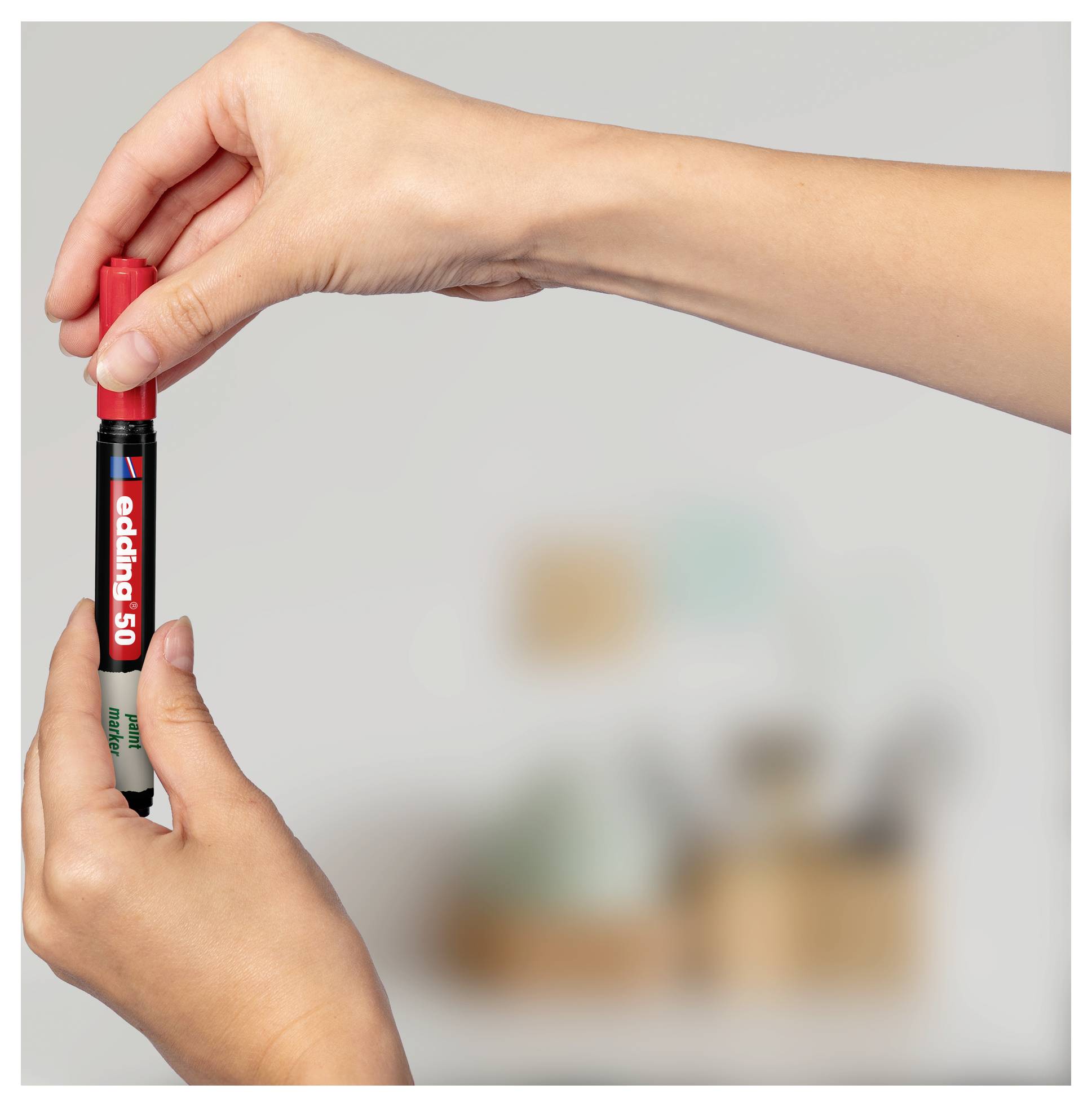 Hände, die einen schwarzen Marker mit roter Kappe aufrecht gegen einen unscharfen Hintergrund halten.