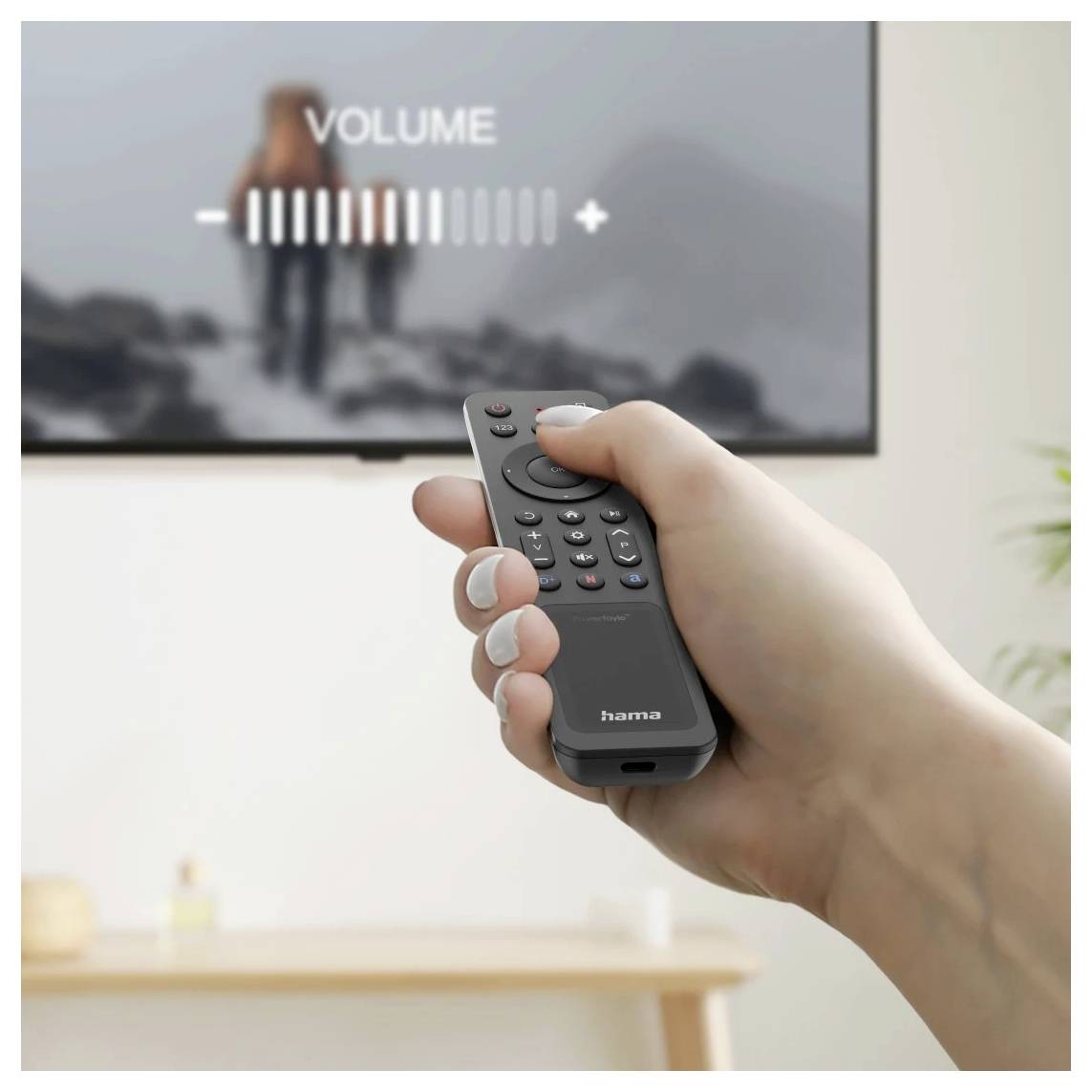 Hand hält eine Fernbedienung, während die Lautstärke auf einem Fernsehbildschirm eingestellt wird, auf dem „VOLUME" mit einer Balkenanzeigu angezeigt wird
