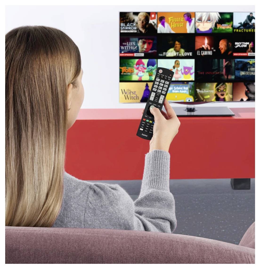 Eine Frau schaut auf einen TV-Streaming-Startbildschirm und hält eine Fernbedienung in der Hand, während sie auf einem Sofa sitzt.