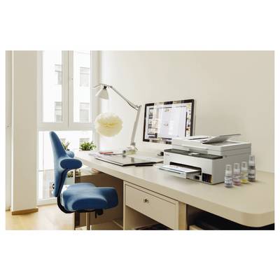 Helles Homeoffice mit blauem Stuhl, Schreibtisch, Computer, Drucker, Lampe und Zubehör neben einem Fenster.